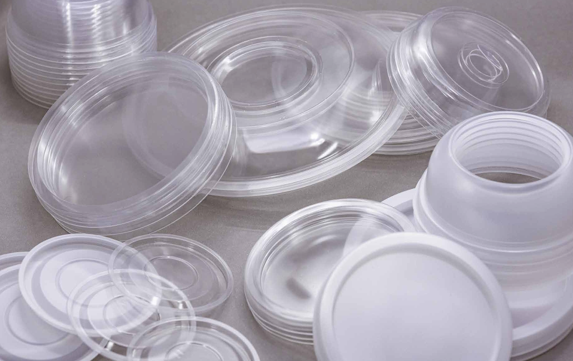 Montones y pilas de tapas de plástico transparentes y blancas para recipientes, esparcidas sobre una superficie gris.