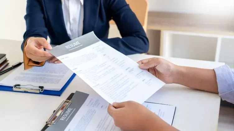 A woman is giving a resume to a man at a job interview.