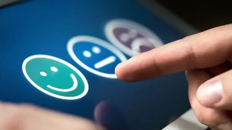 A person is pointing at three smiley faces on a tablet.