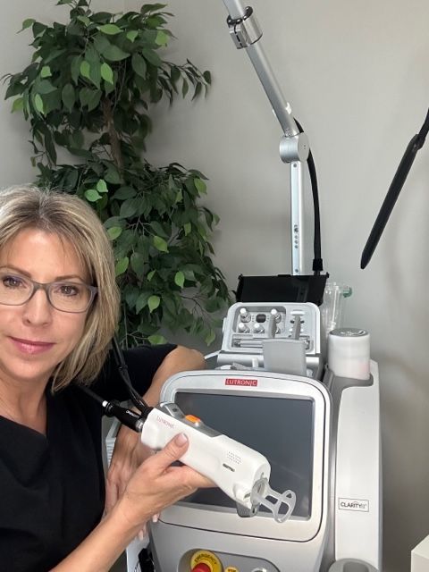 Woman posing beside a medical laser device in a clinic, holding its handpiece.