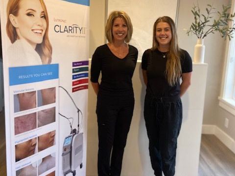 Two women standing beside a skincare display in a bright room, smiling at the camera.