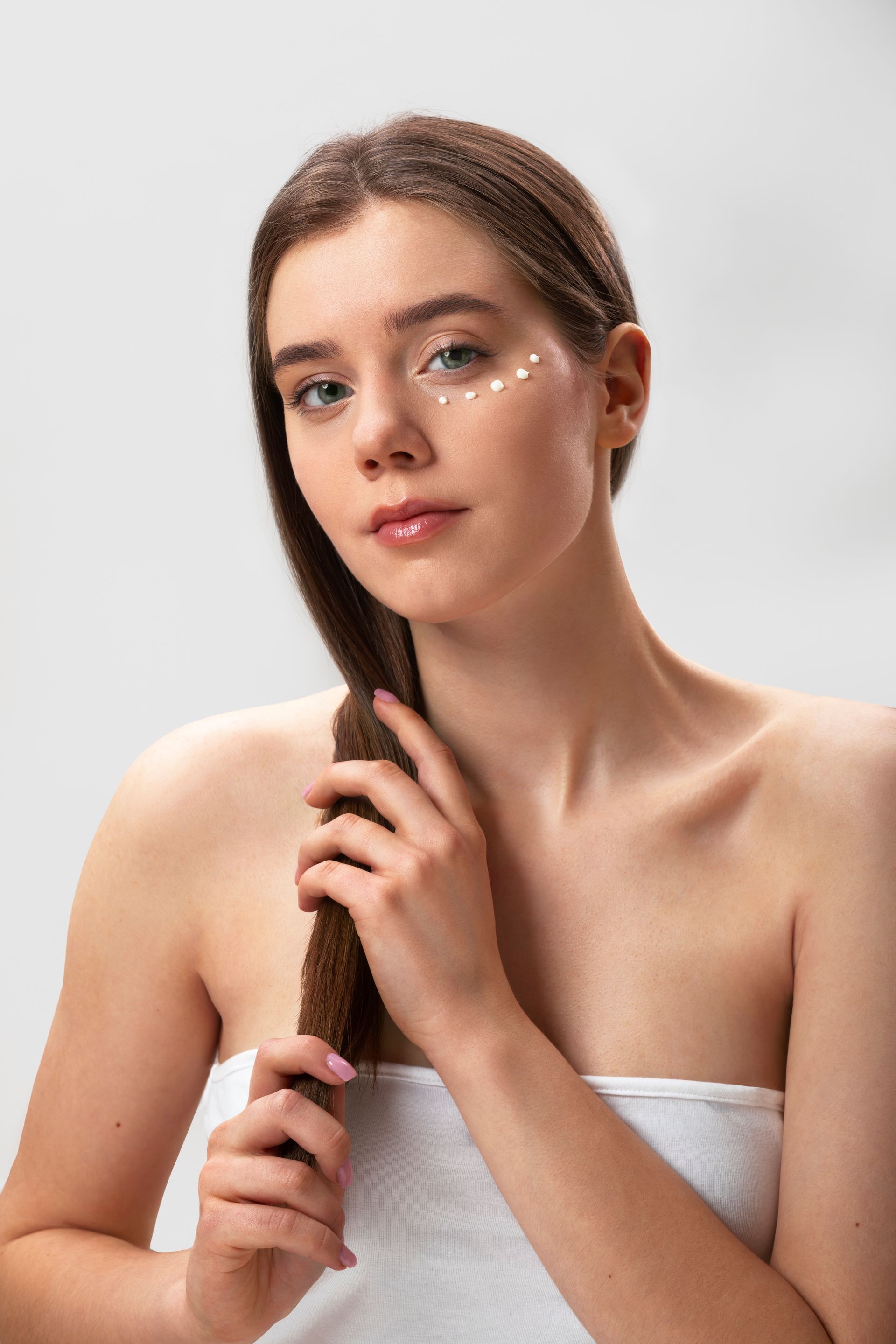 Portrait of a woman with wet hair against a light gray background, wearing a white towel and holding a braid