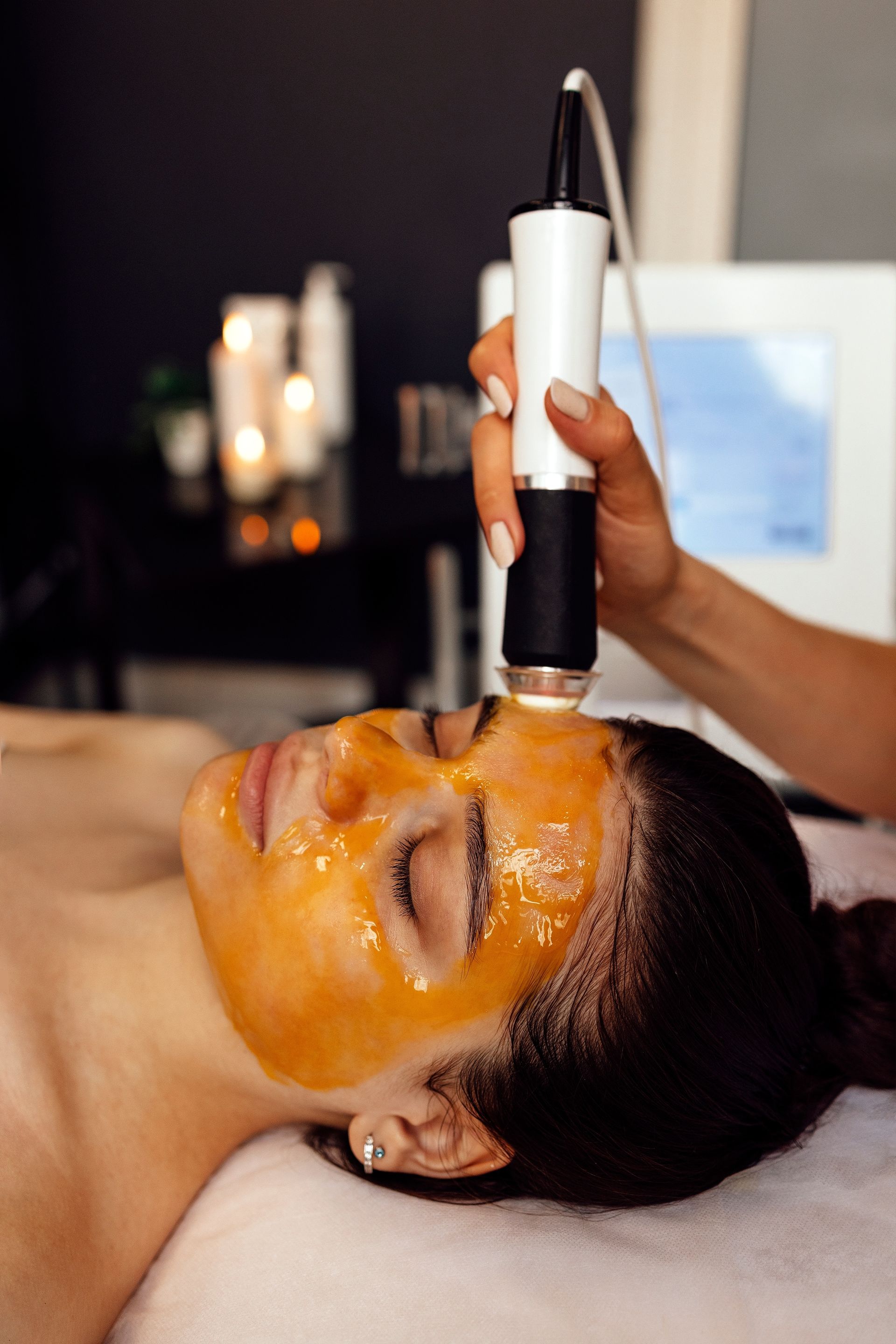 Facial treatment with orange mask applied using a handheld device on a client’s face