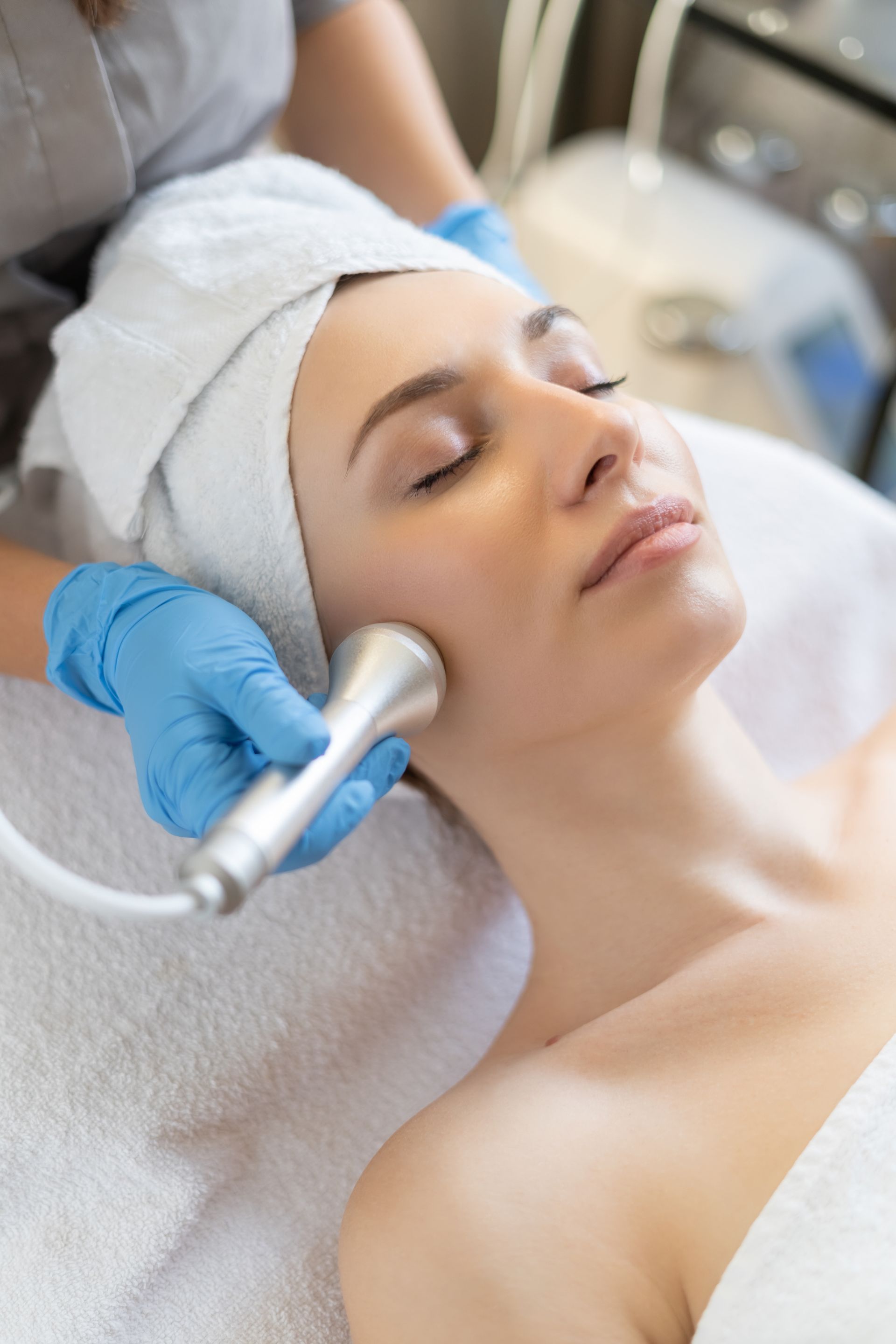 Spa treatment with gloved esthetician using a handheld device on a relaxed client’s face