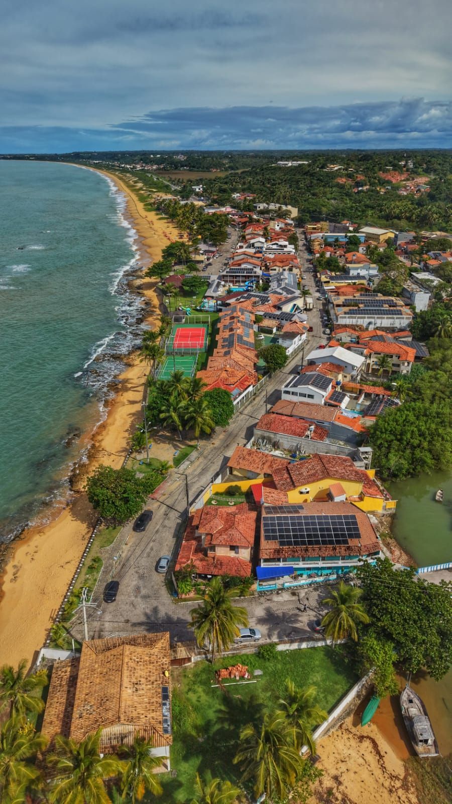 Vista aérea de uma cidade costeira com casas coloridas, praia e oceano sob um céu nublado.
