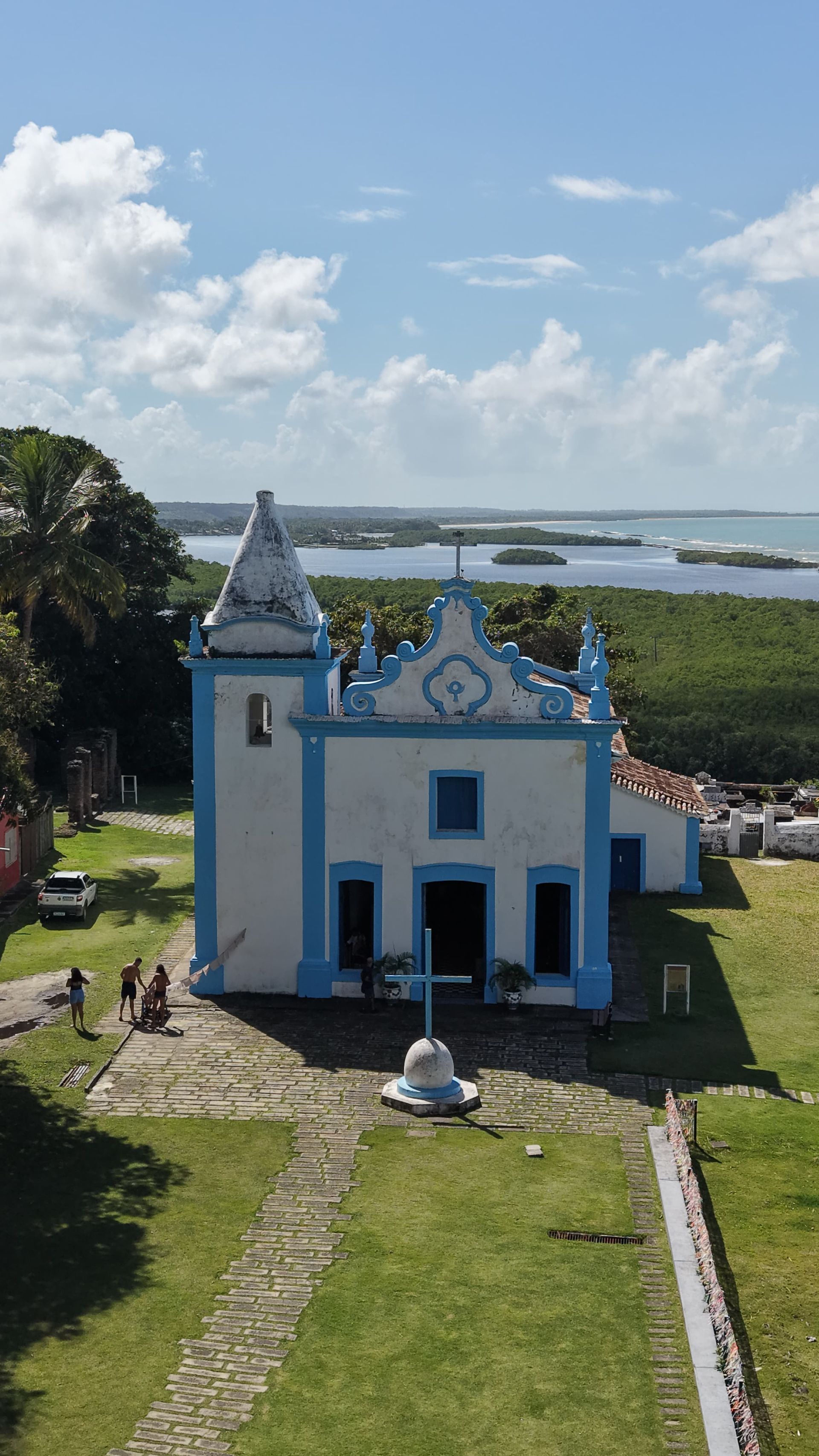 Pequena capela branca e azul em uma colina gramada com vista para o oceano sob um céu claro.