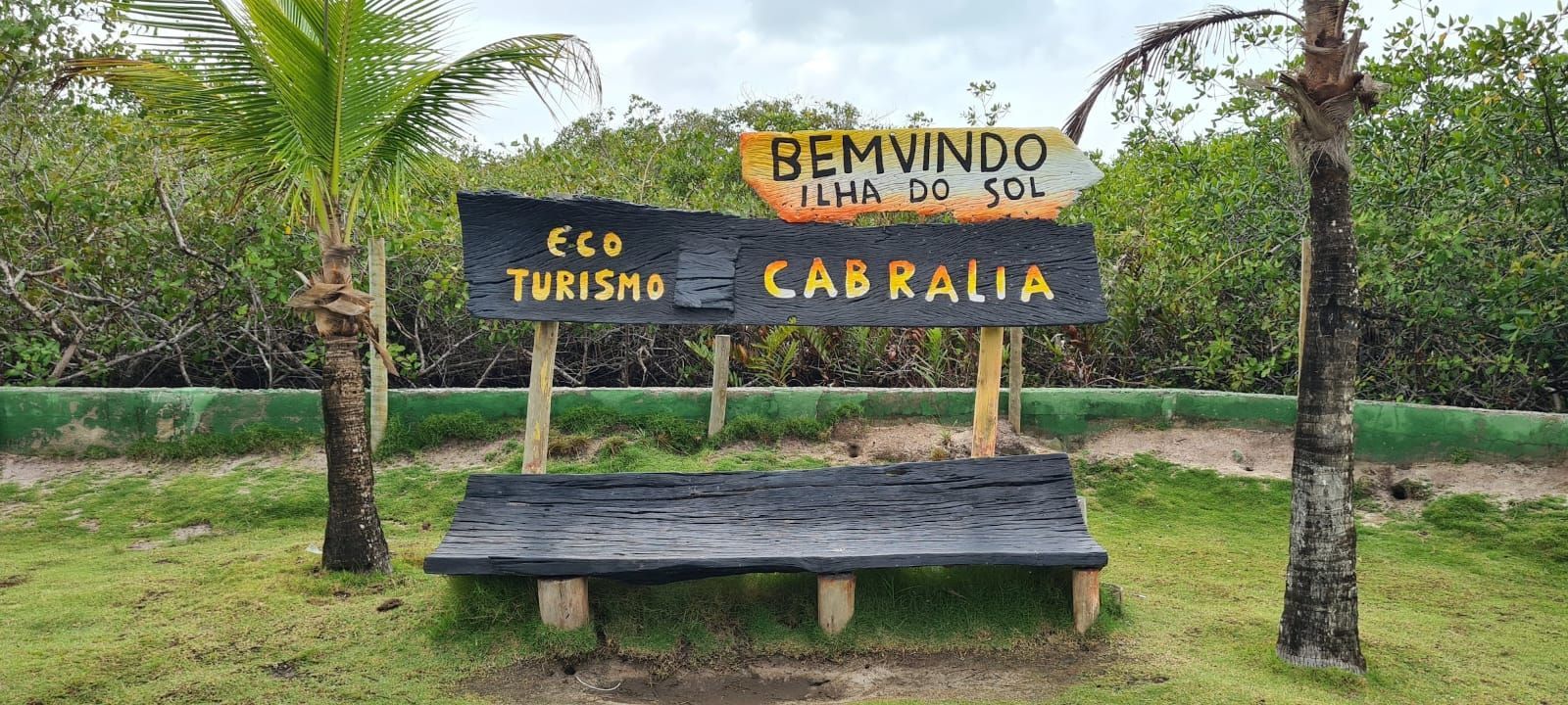 Placa de madeira de boas-vindas para a Eco Turismo Cabralia em um cenário verdejante à beira da estrada.