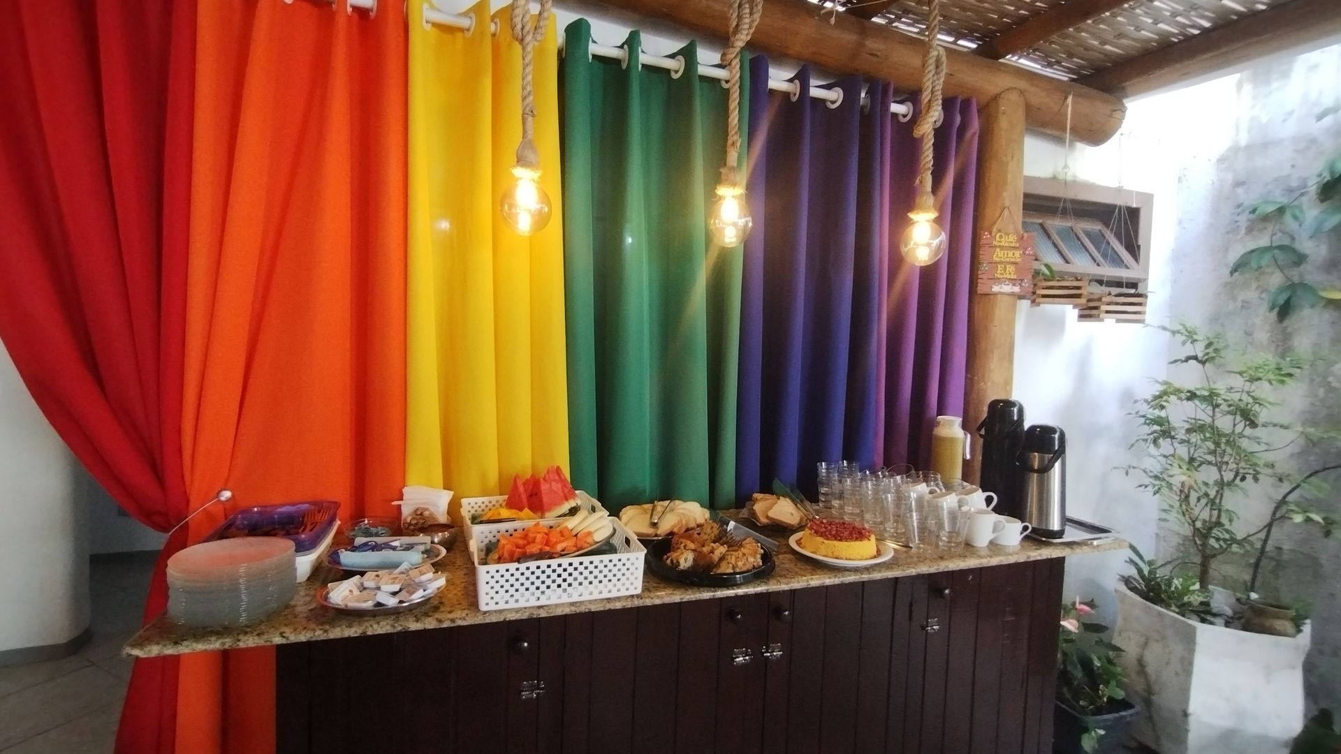 Cortinas coloridas e drapeadas atrás de uma mesa com comida e bebida em uma reunião decorada.