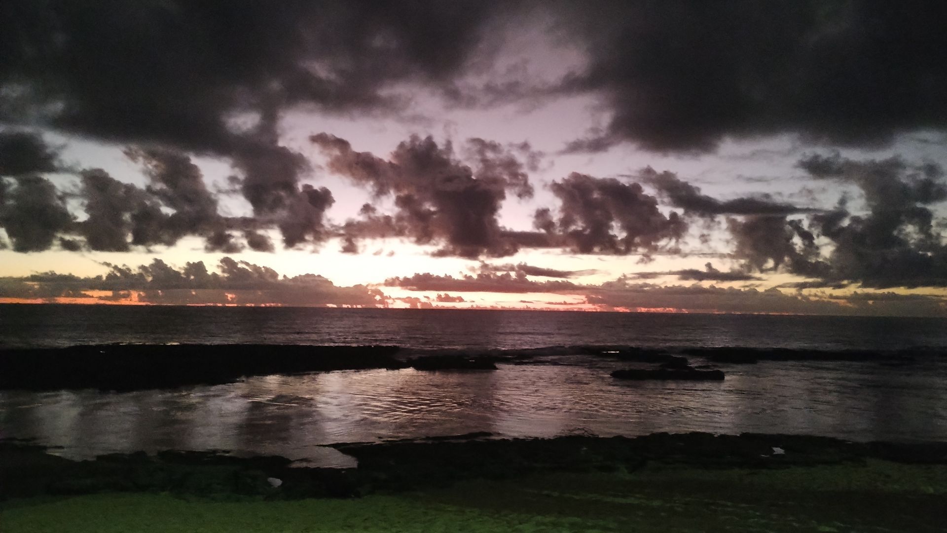 Pôr do sol sobre uma superfície de água calma, com nuvens escuras e um horizonte brilhante.