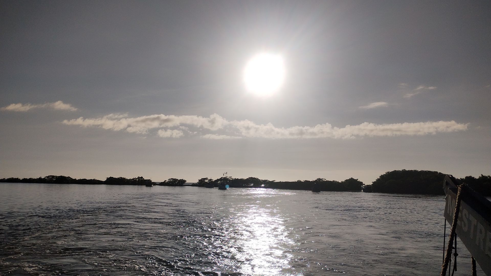 Oceano ensolarado com águas ondulantes, costa distante e sol brilhante baixo no céu.