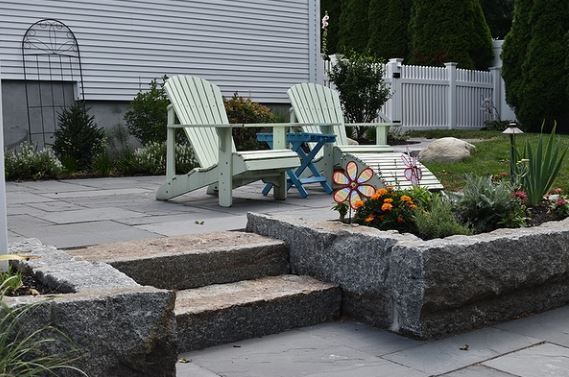 Stone patio with round table and stools in a landscaped garden with rocks and shrubs
