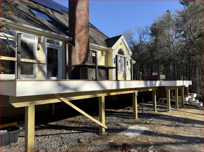 House raised on wooden stilts with a brick chimney and deck in a wooded yard