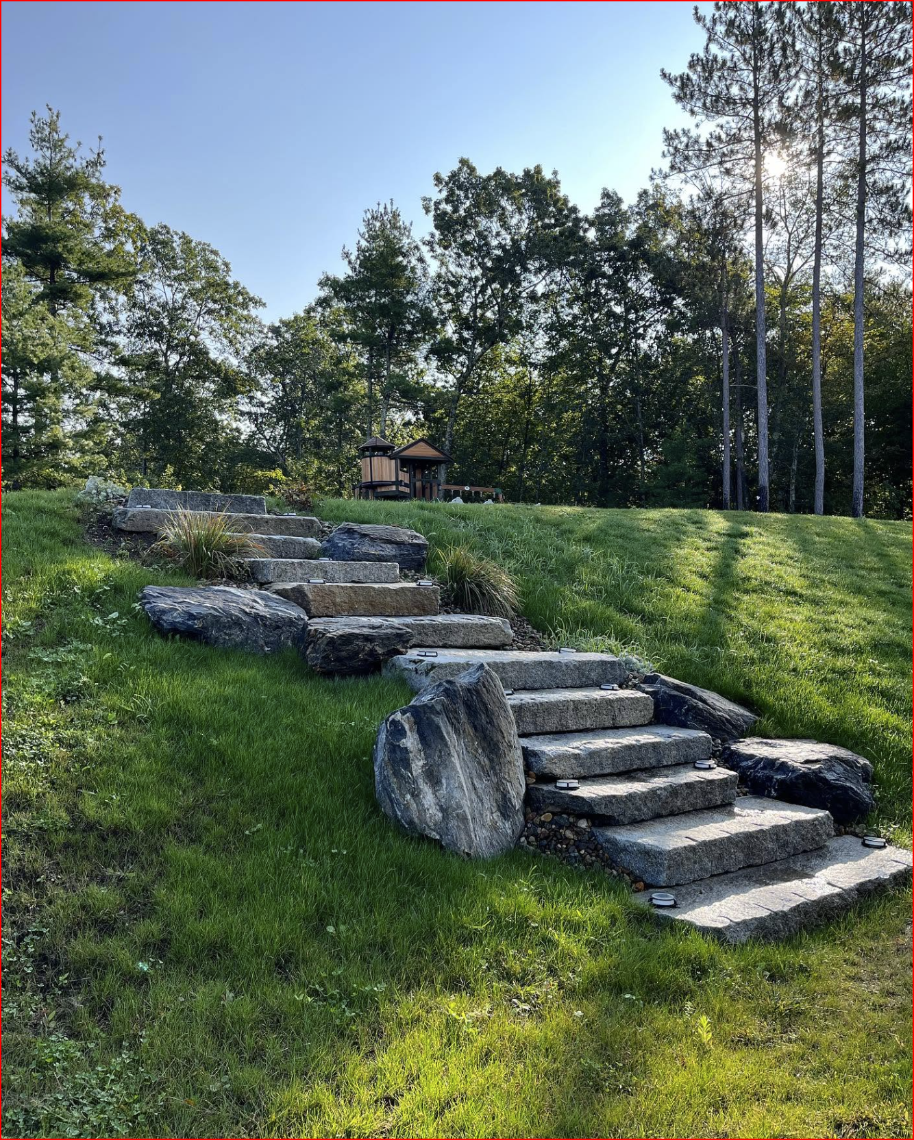 Backyard garden with stone path, log steps, mulch beds, shrubs, and a wooden fence