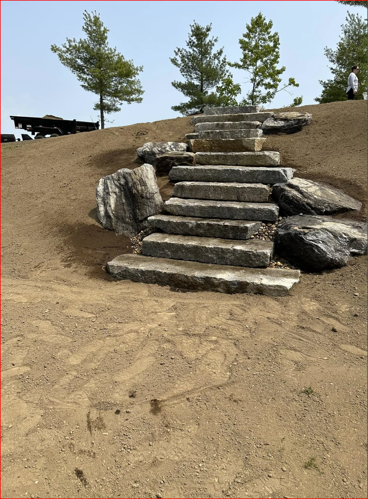 Rock garden with large stones, mulch, trees, and a wooden fence in a landscaped yard