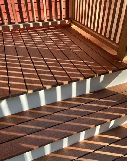 Wooden porch steps and railing casting strong striped shadows in warm sunlight.