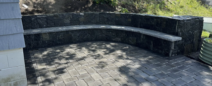 Curved stone bench in a paved outdoor patio beside a wall and greenery