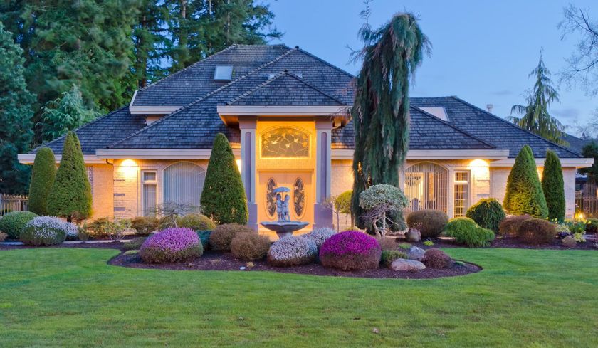 A large house with a fountain in front of it is lit up at night.