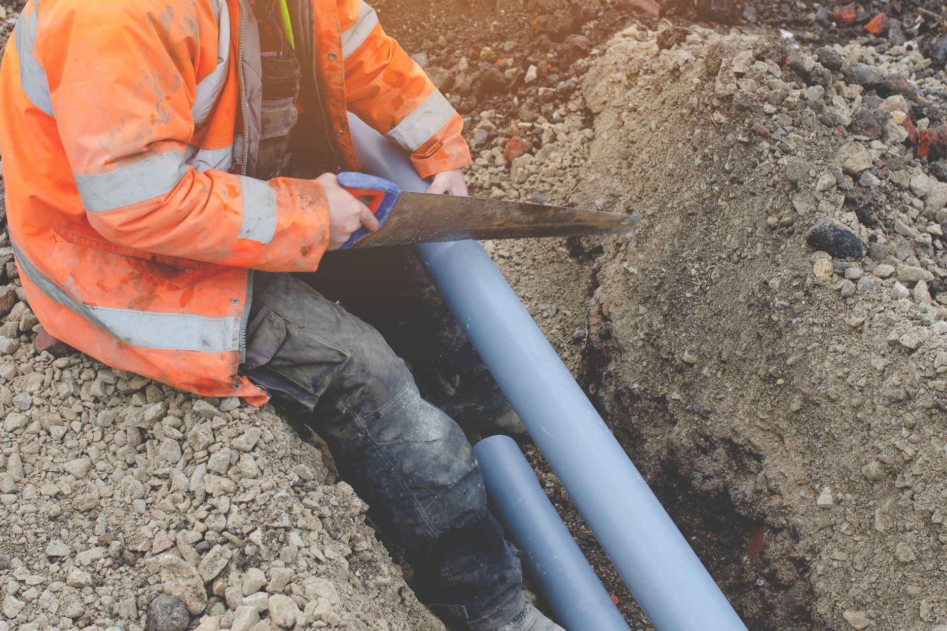 A Man is Cutting a Pipe with a Saw in the dirt — Peoria, IL — Rooter-Matic Sewer Drain and Septic A Man is Cutting a Pipe with a Saw in the dirt — Peoria, IL — Rooter-Matic Sewer Drain and Septic