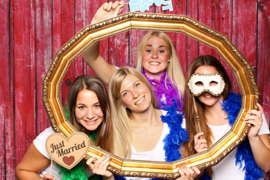 Four people posing in a gold frame booth with props against a pink wooden backdrop