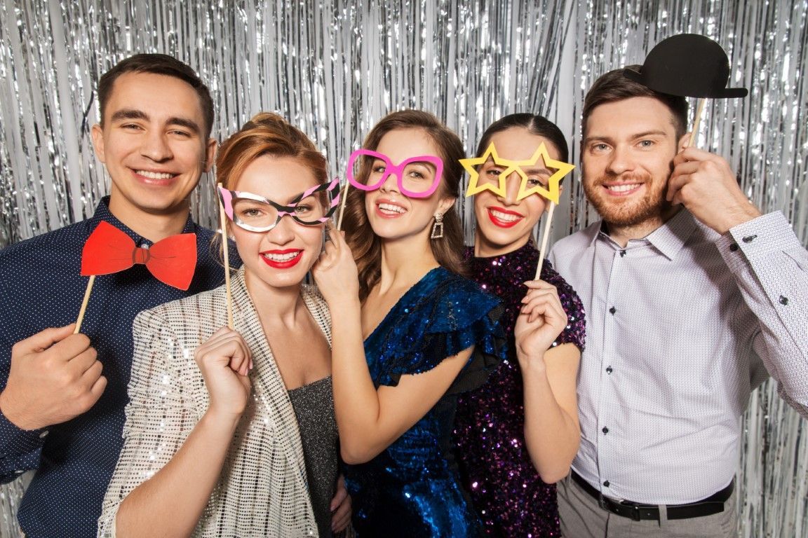 Five friends posing in party props before a silver tinsel backdrop