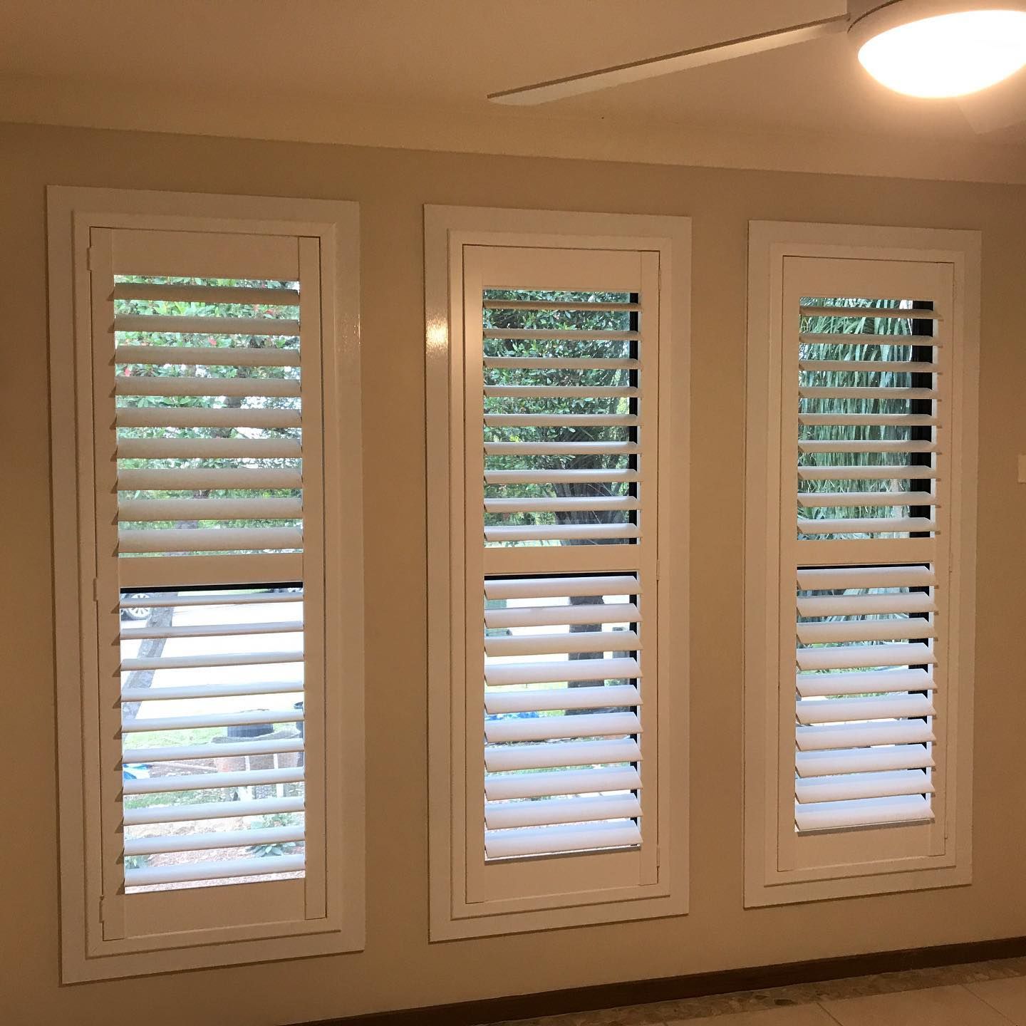 Three White Shuttered Windows in a Room With Beige Walls and a Ceiling Fan — BlindDESIGN in Byron Bay, NSW