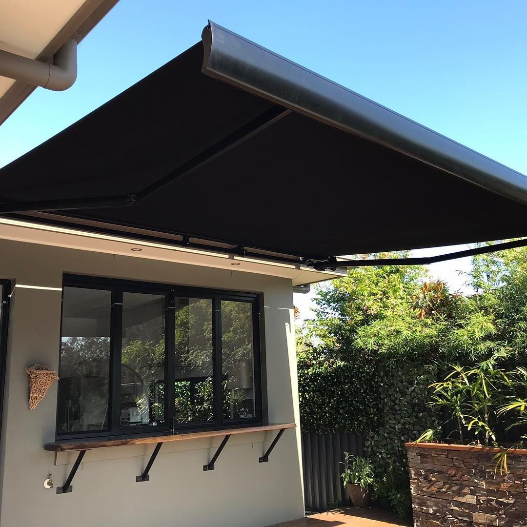 Black Retractable Awning Over a Window With a Wooden Bar and a Grey Wall — BlindDESIGN in Tweed Heads, NSW