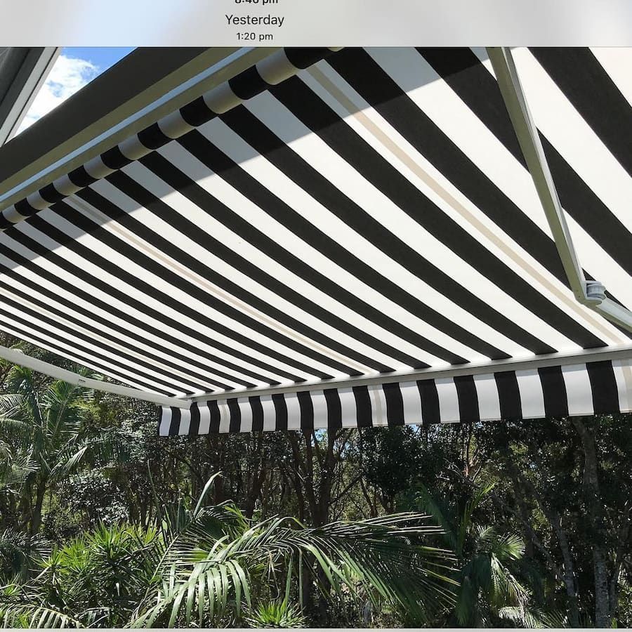 Black and White Striped Awning Extending Over Green Foliage — BlindDESIGN in Tweed Heads, NSW
