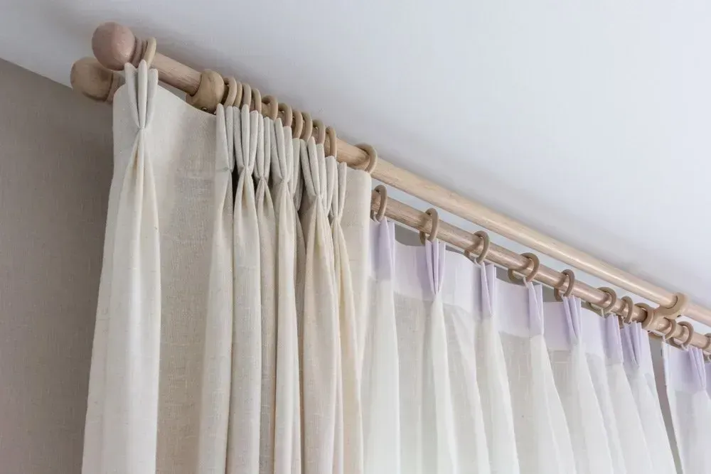 Natural linen pinch pleat curtains Byron Bay installation on a timber curtain rod with wooden ring carriers and ball finial