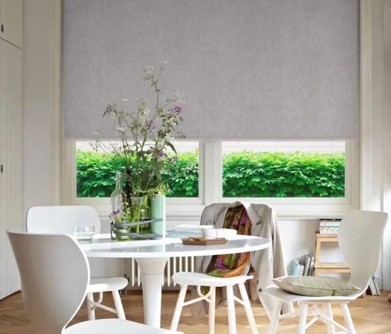 Automated roller blinds partially lowered over window in a modern dining room setting