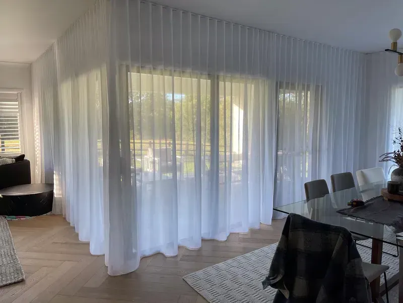 Floor-to-ceiling sheer white curtains across a large living and dining room window wall.