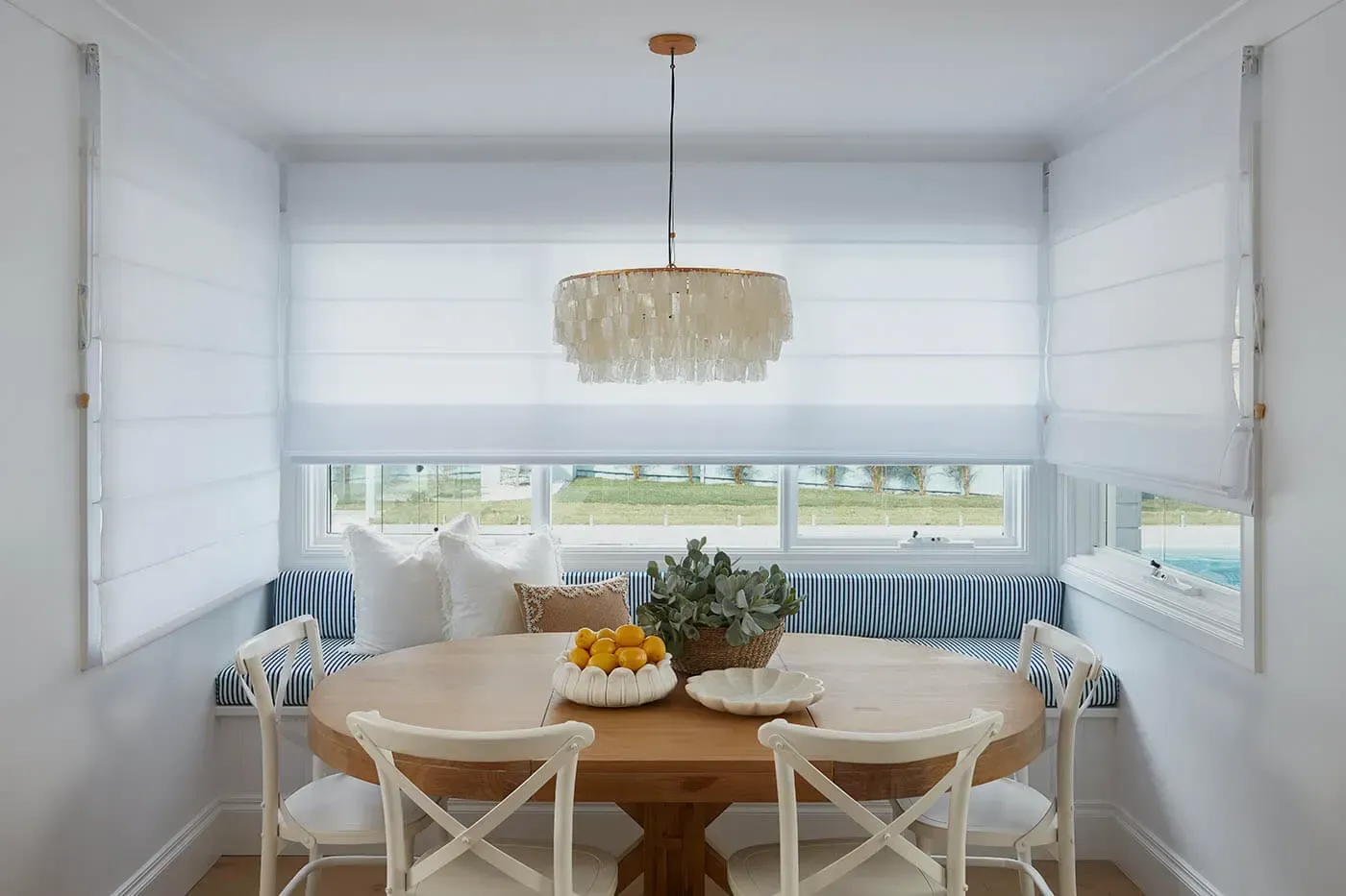 Cozy Dining Nook With Round Wooden Table, White Chairs, and Bench With Blue Striped Cushions — BlindDESIGN in Byron Bay, NSW