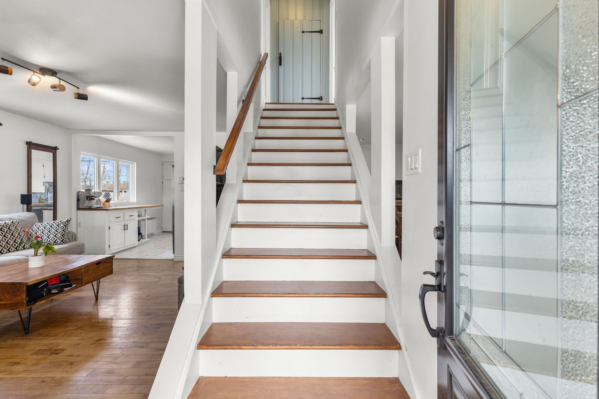 Escalier menant à une porte fermée, visible depuis l'entrée principale d'une maison.