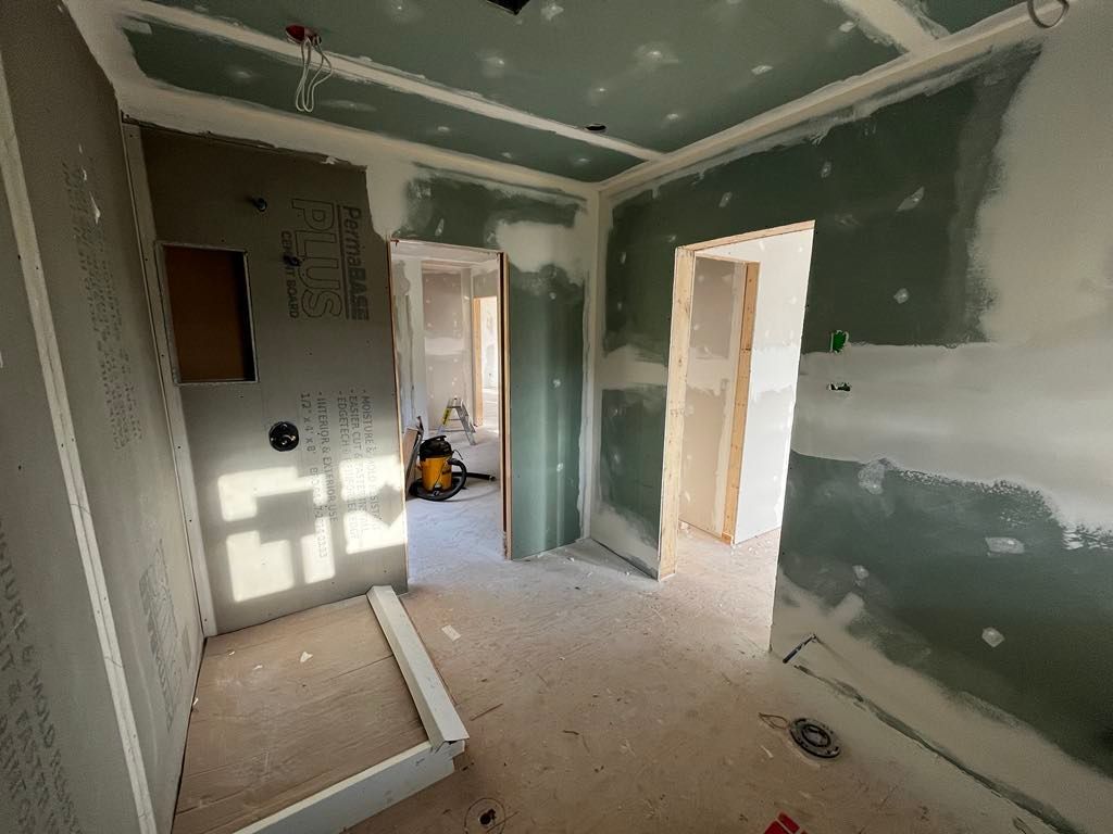 Intérieur d'une pièce en construction, avec des cloisons sèches vertes, des portes et un plafond inachevé.