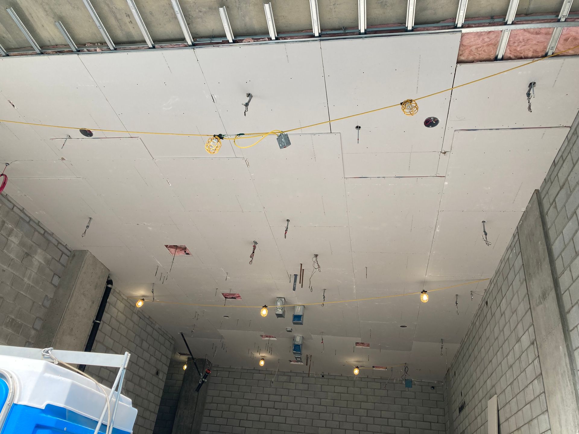 Chantier intérieur avec câblage apparent et éclairage au plafond. Murs en briques blanches.