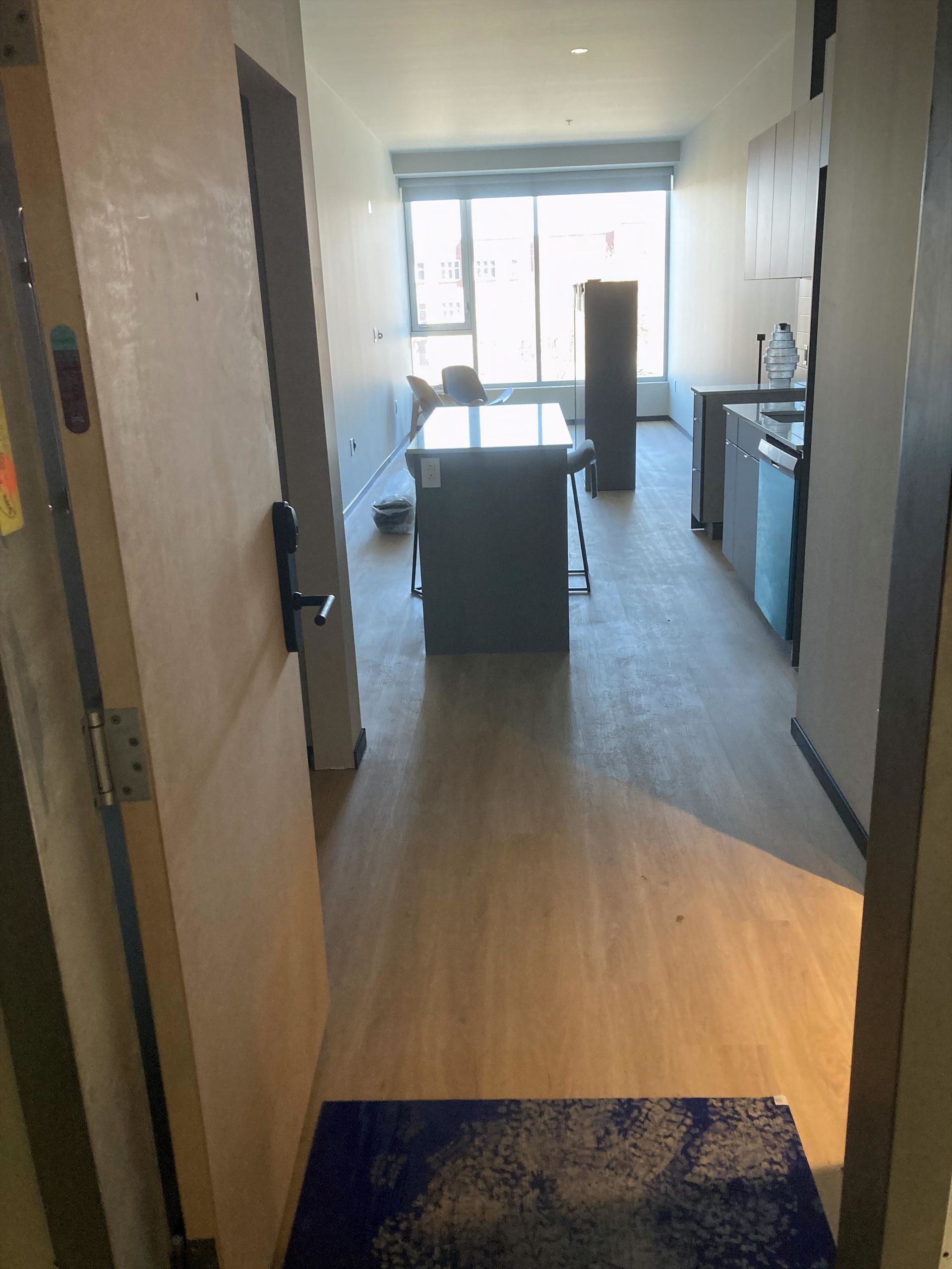 Porte ouverte donnant sur un appartement avec parquet, îlot central et fenêtres.