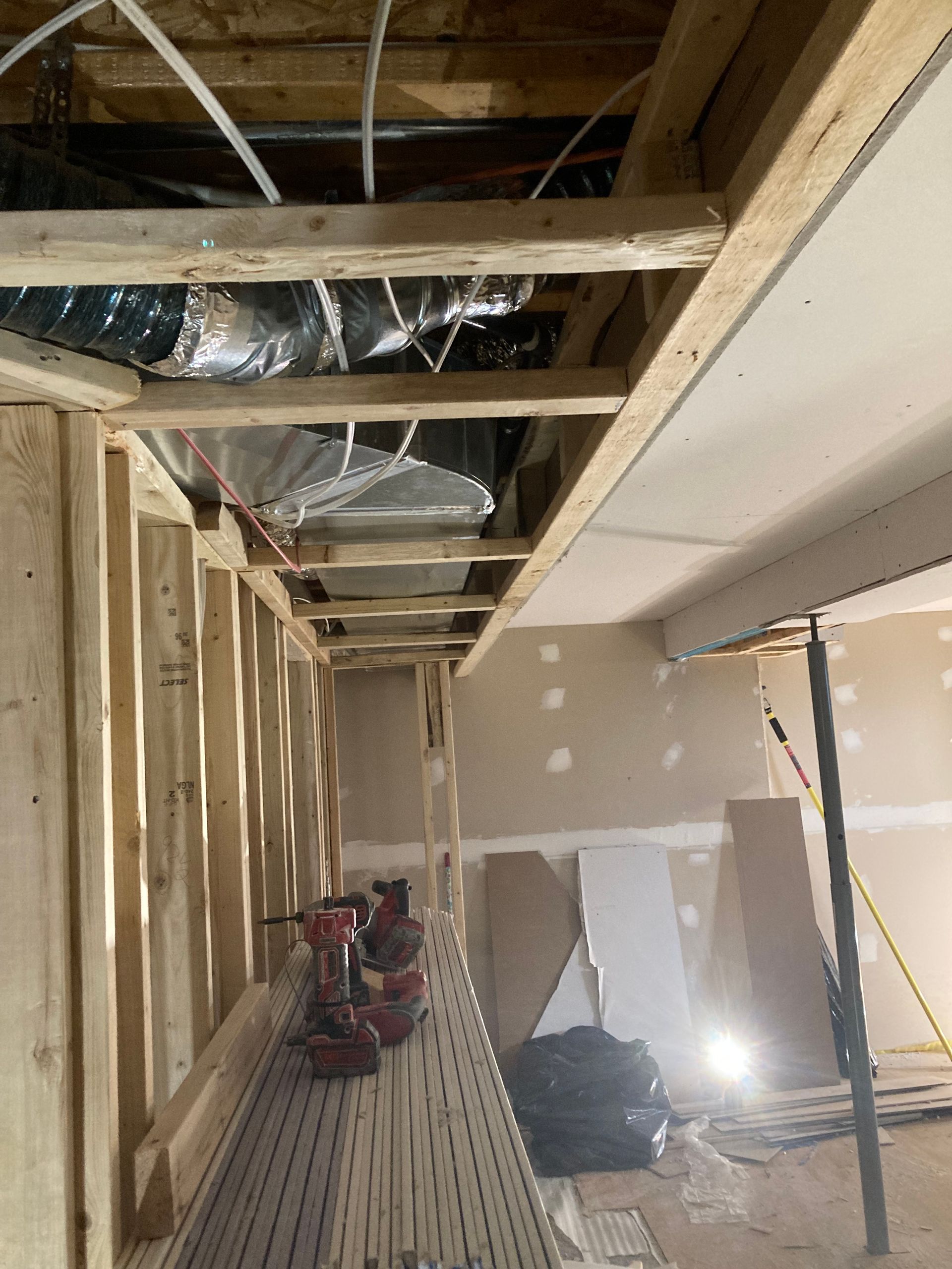 Chantier de construction intérieur. Charpente en bois apparente, conduits de ventilation, cloisons sèches, outils et poutres de soutien.