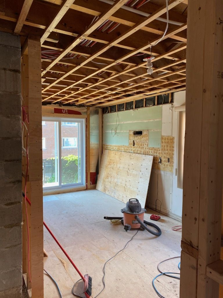 Pièce intérieure en cours de rénovation, solives de plafond apparentes, montants en bois, cloisons sèches, aspirateur et porte coulissante en verre.