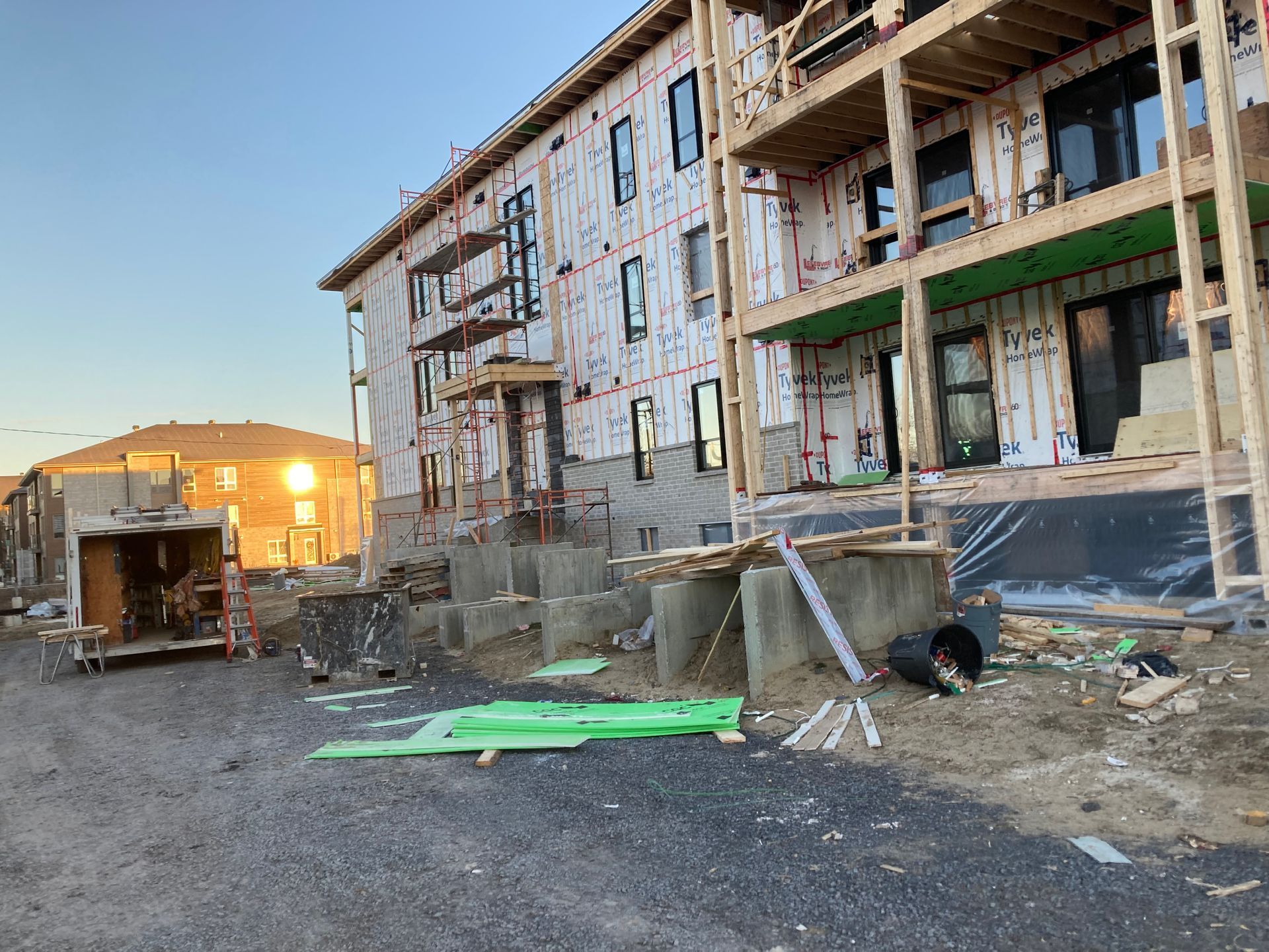 Chantier : structure d’un immeuble de plusieurs étages avec isolation. Niveau du sol, débris et bâtiment en arrière-plan.