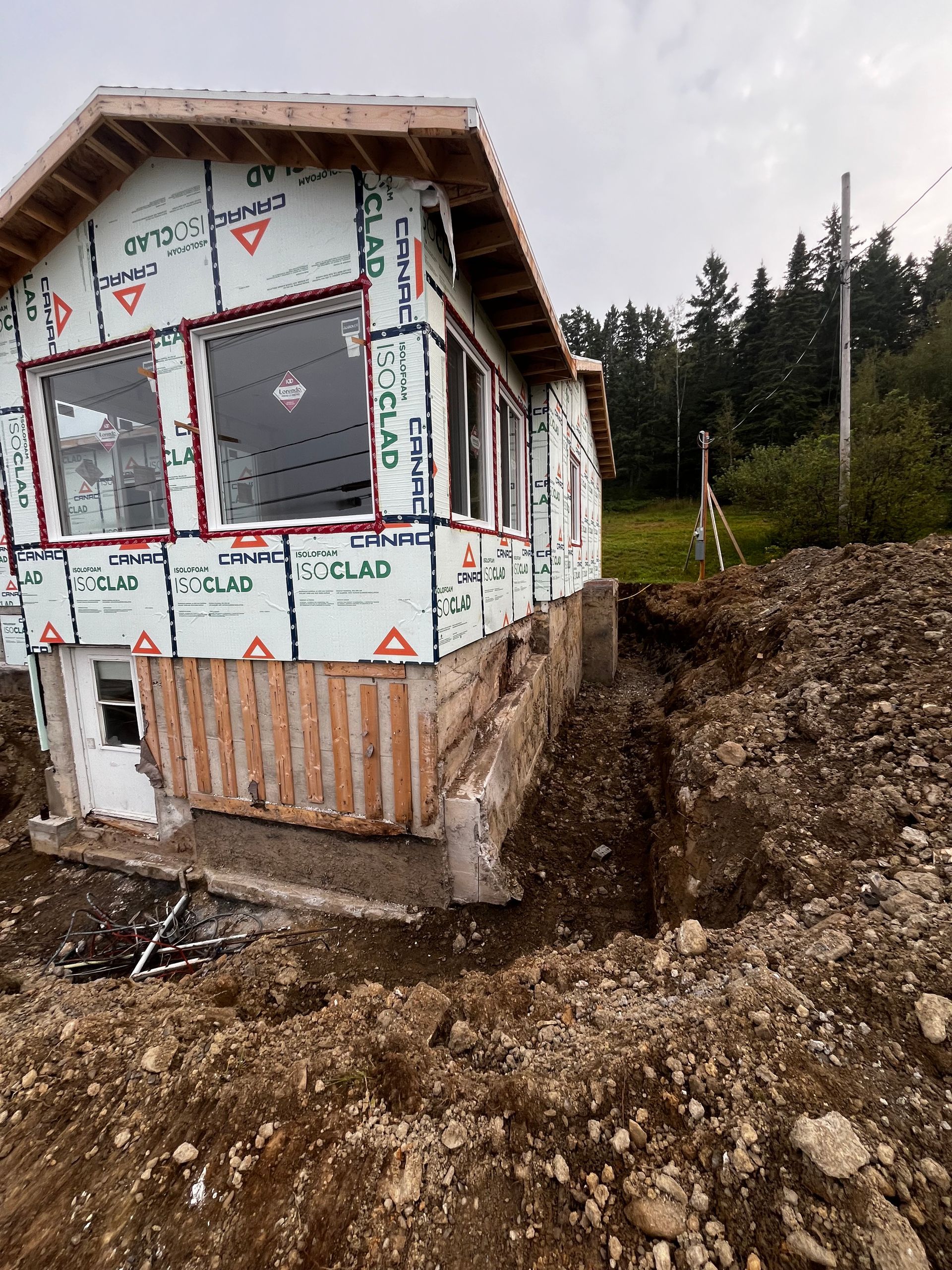 Maison en construction avec charpente en bois apparente, pare-vapeur et fossé de fondation.