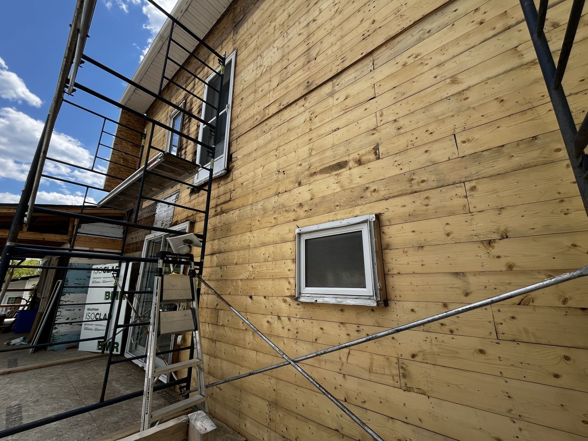 Maison en bois en construction, façade en bois, échafaudages présents, ciel bleu dégagé.