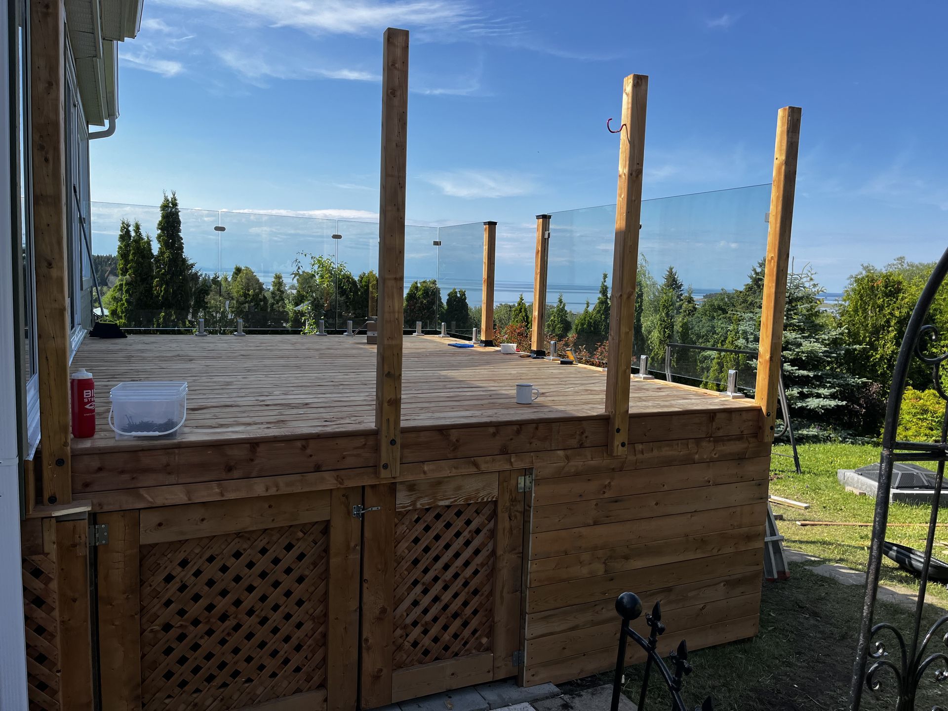 Terrasse en bois en construction avec rambarde et poteaux en verre, donnant sur l'eau.