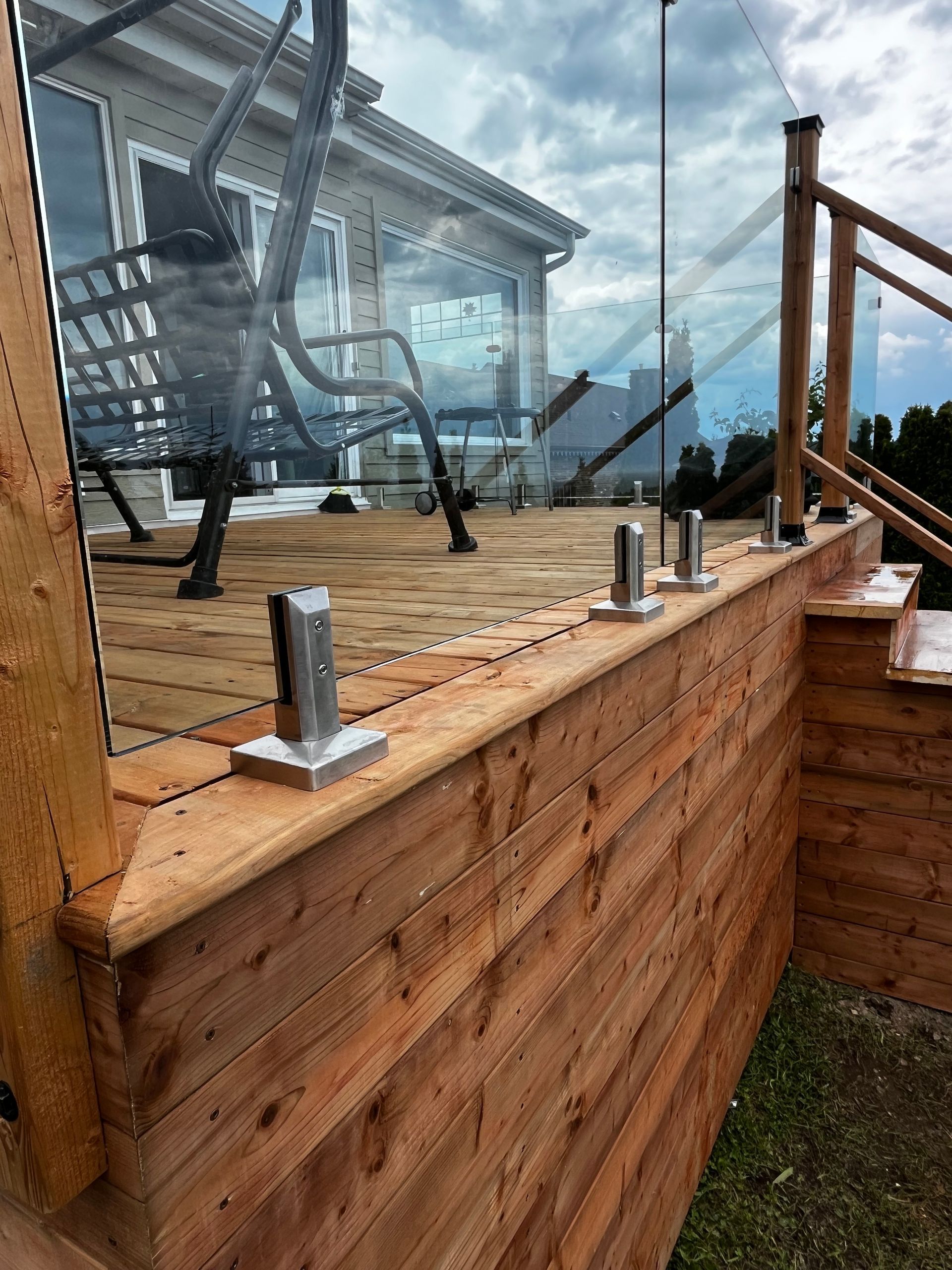 Terrasse en bois avec rambarde en verre et poteaux en acier inoxydable. Une balançoire noire est installée sur la terrasse.