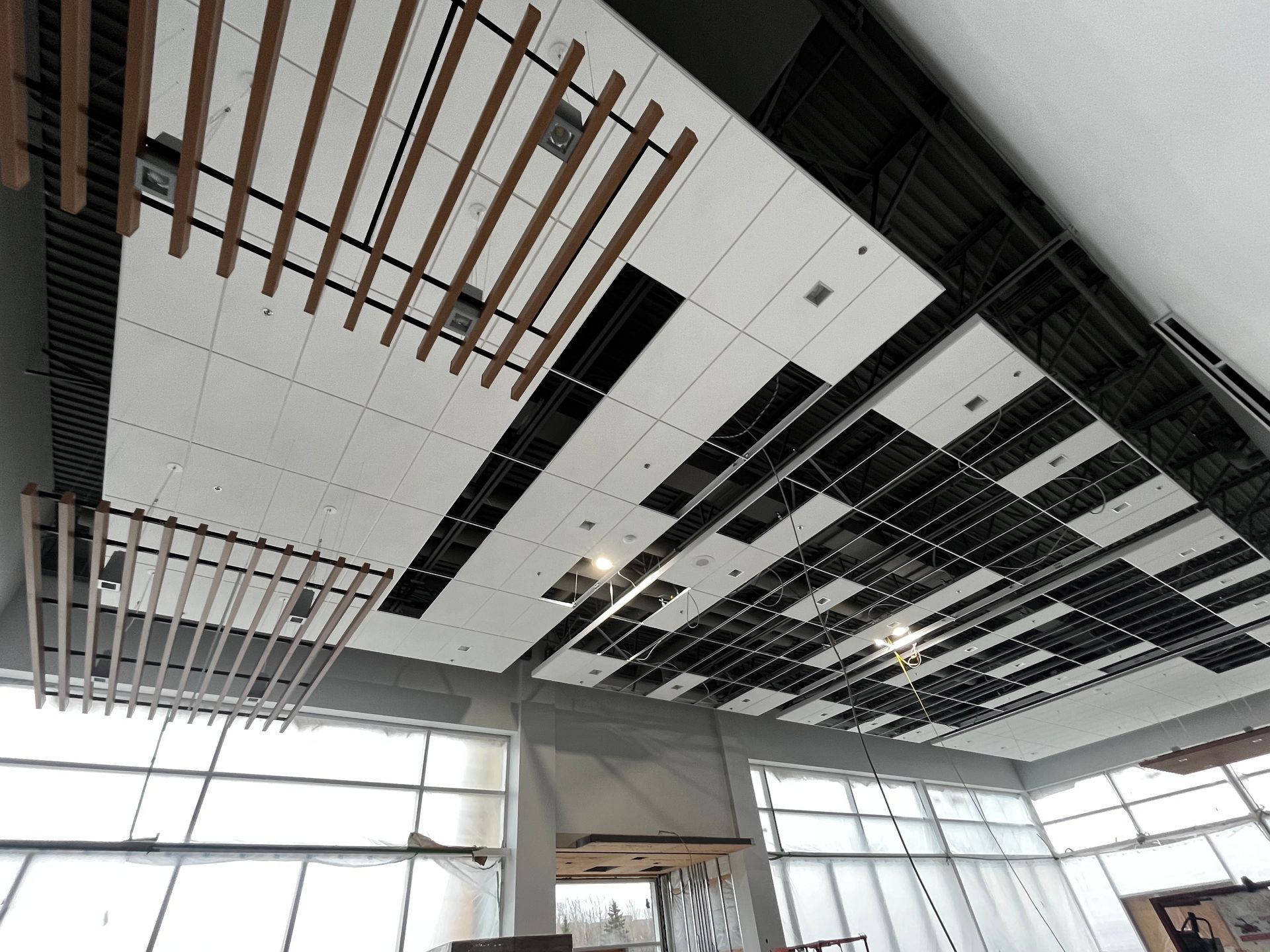 Plafond en construction avec poutres en bois et panneaux blancs, près des fenêtres.
