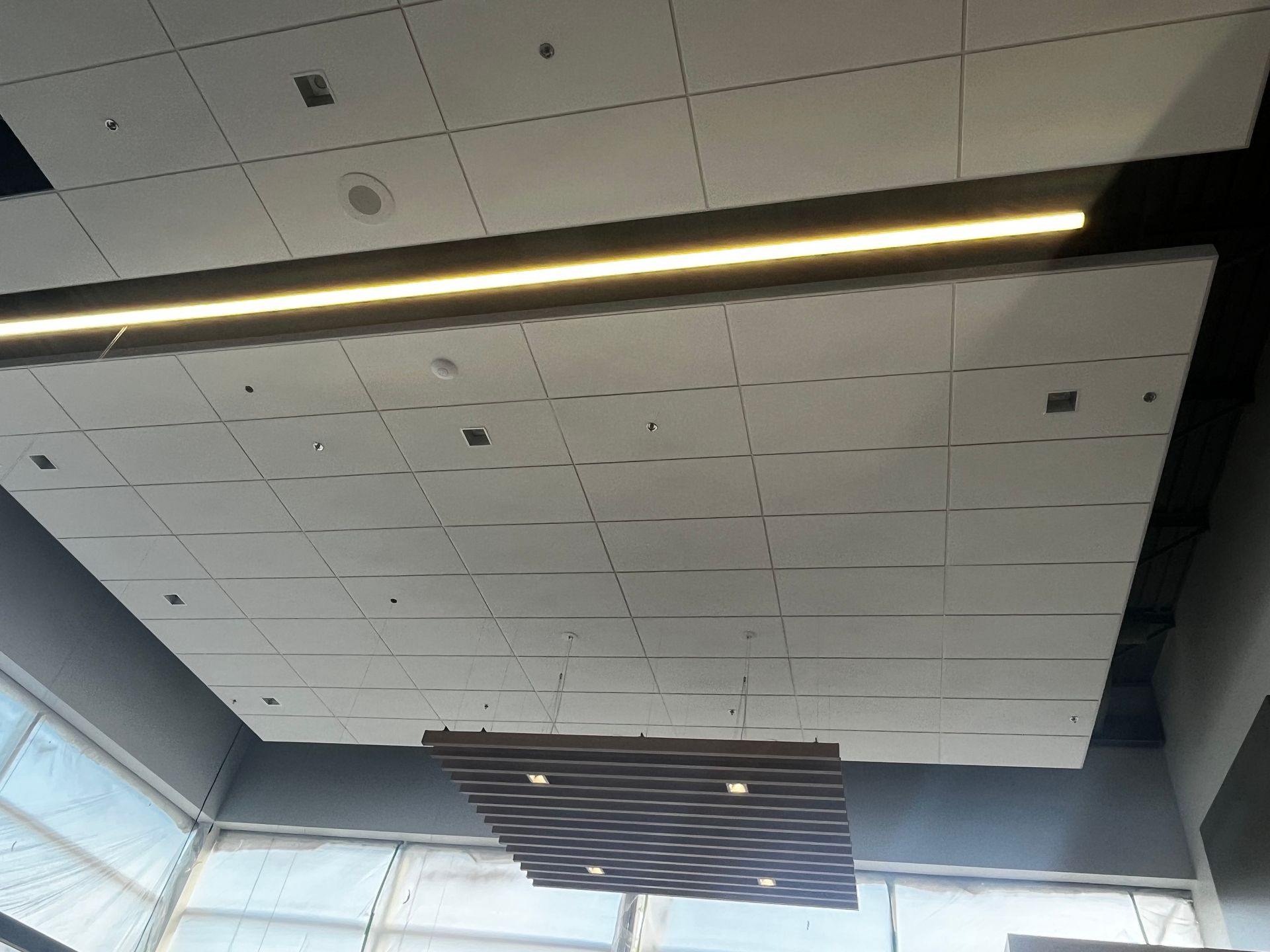 Dalles de plafond blanches avec luminaire linéaire et panneau décoratif.