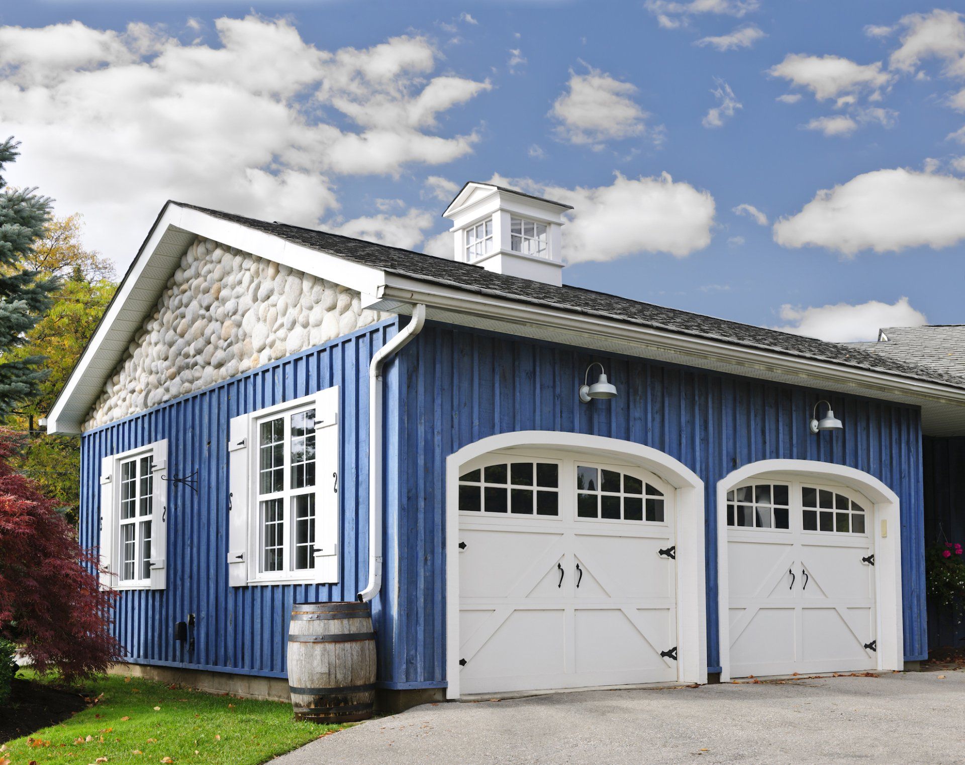Garage aux murs bleus avec deux portes cintrées blanches, accents de pierre, moulures blanches et une petite coupole sous un ciel partiellement nuageux.