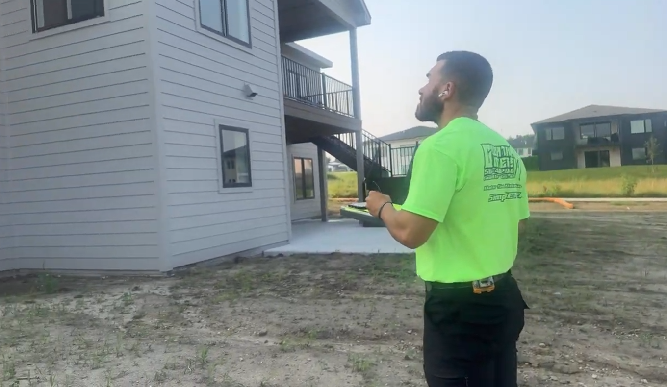 Man in neon green shirt looking up at a building, holding a clipboard outside.