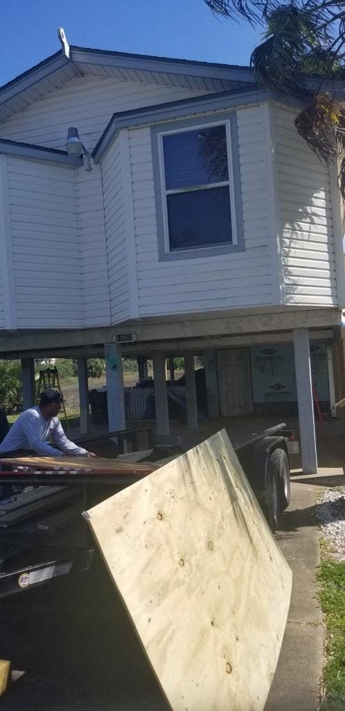A man is carrying a large piece of wood in front of a house.