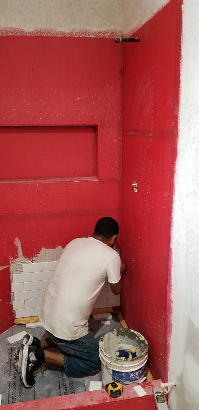 A man is kneeling down in a bathroom with red walls.