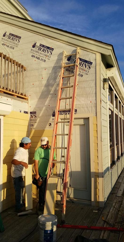 Two men are standing in front of a building with a ladder.