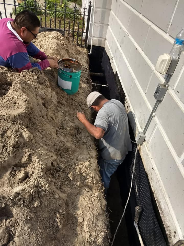 Two men are working on the side of a building in the dirt.